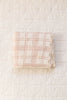 The Organic Cotton Baby Blanket - French Plaid, Petal, featuring pale pink and cream plaid and lace trim, is folded on a white diamond-quilted surface.