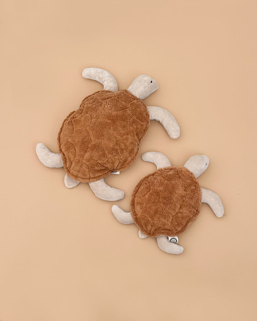 Two Senger Naturwelt Cuddly Animal Turtles, one large and one small, with brown shells and light flippers, rest on a plain beige background. Made from organic cotton and inspired by Senger Naturwelt's heat pad design.