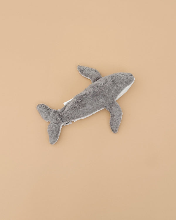 The Senger Naturwelt Cuddly Animal - Whale, a gray plush toy with a white underside made from organic cotton, is displayed on a plain beige background.