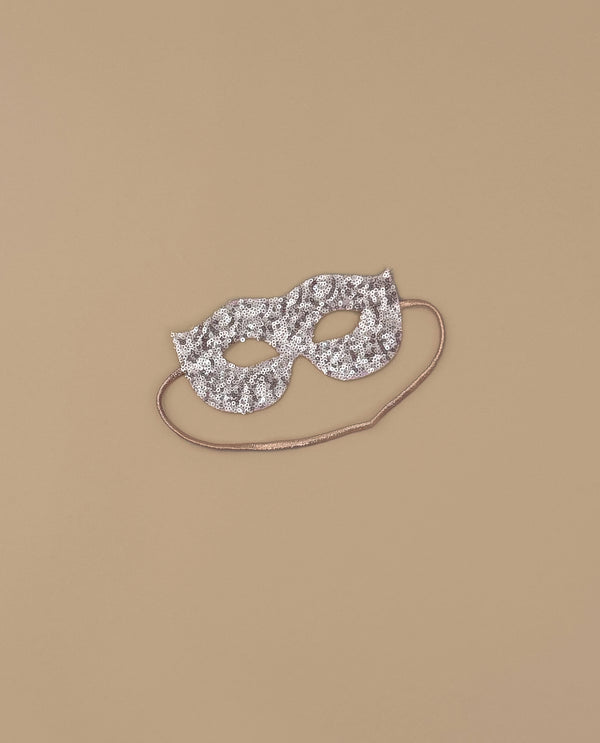 A shimmering pink sequin masquerade mask with eye holes and a thin string—ideal as a costume accessory for glamorous evenings—displayed on a plain beige background.