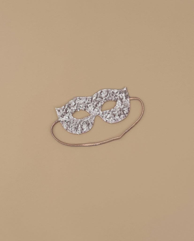 A shimmering pink sequin masquerade mask with eye holes and a thin string—ideal as a costume accessory for glamorous evenings—displayed on a plain beige background.