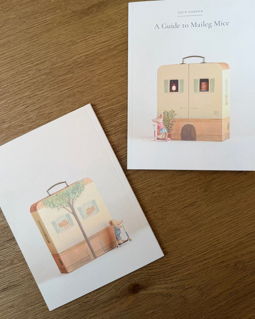 Two illustrated guidebooks from the Odin Parker’s Maileg Catalog featuring Maileg mice playing with scooter toys in front of suitcase-shaped houses.