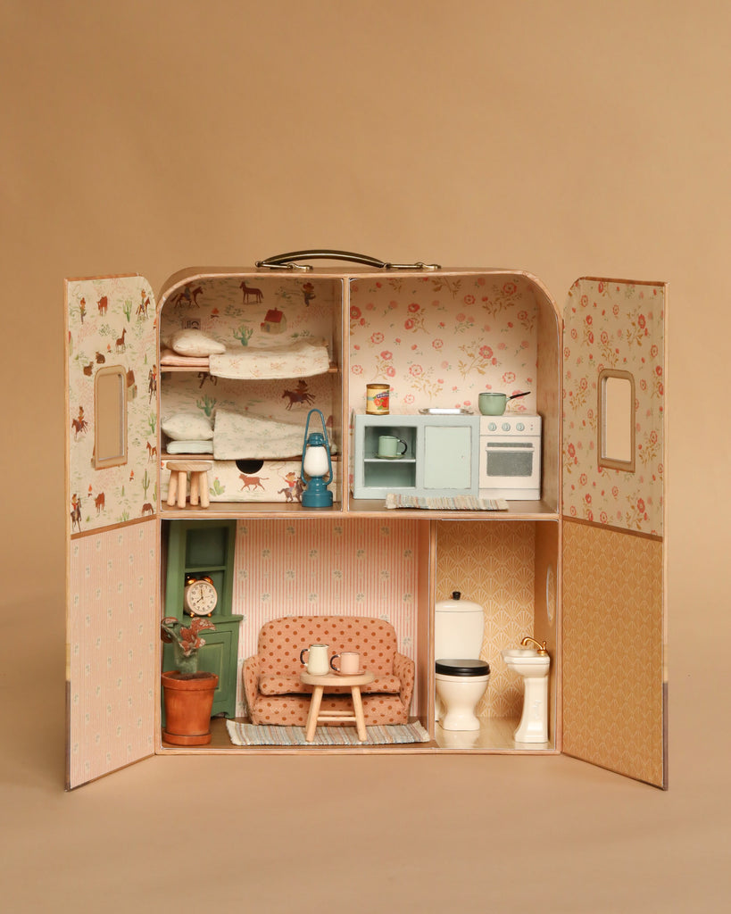 The Maileg Fully Furnished SuitCasa Set is a two-story miniature house with open doors, featuring pastel-decorated rooms: an upstairs bedroom and kitchen, plus a downstairs living room with sofa and a bathroom—all with Maileg furniture.