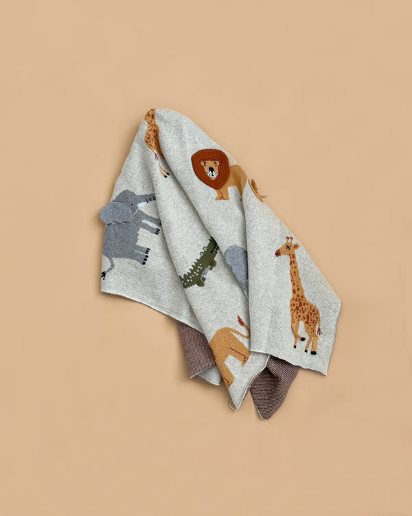 The Organic Cotton Knit Baby Blanket - Jungle features a light gray 100% cotton design with safari animal illustrations—including lion, elephant, giraffe, and crocodile—on a neutral beige background.
