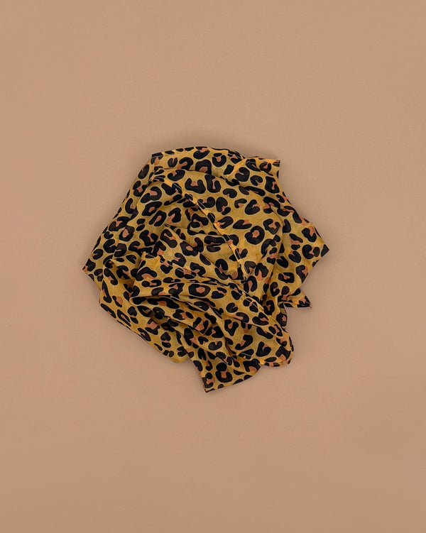 A crumpled piece of cheetah-print fabric in brown, black, and tan on a light brown background—perfect as Sarah's Silks Animal Print Playsilk - Cheetah for Waldorf toys and imaginative play.