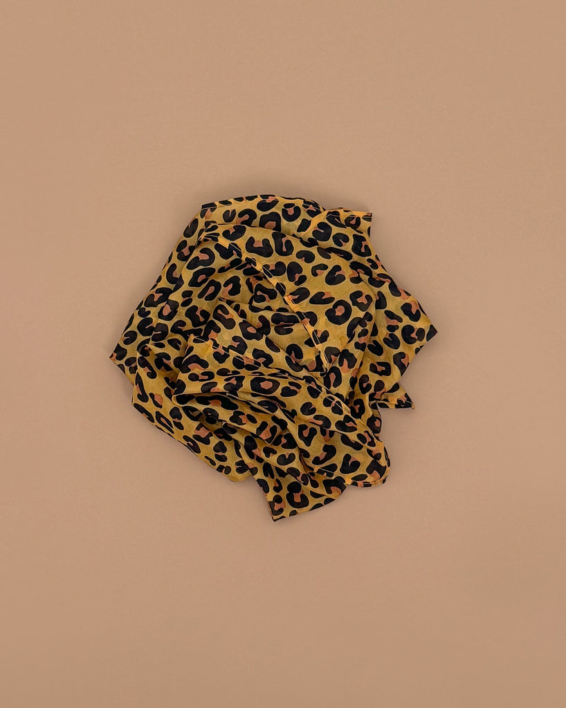 A crumpled piece of cheetah-print fabric in brown, black, and tan on a light brown background—perfect as Sarah's Silks Animal Print Playsilk - Cheetah for Waldorf toys and imaginative play.