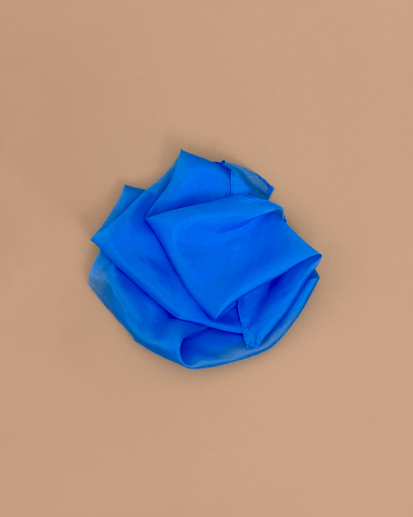 A crumpled Sarah's Silks Solid Color Playsilk - Royal is arranged in a rough circular shape on a plain light brown background, inviting open-ended play and creativity.