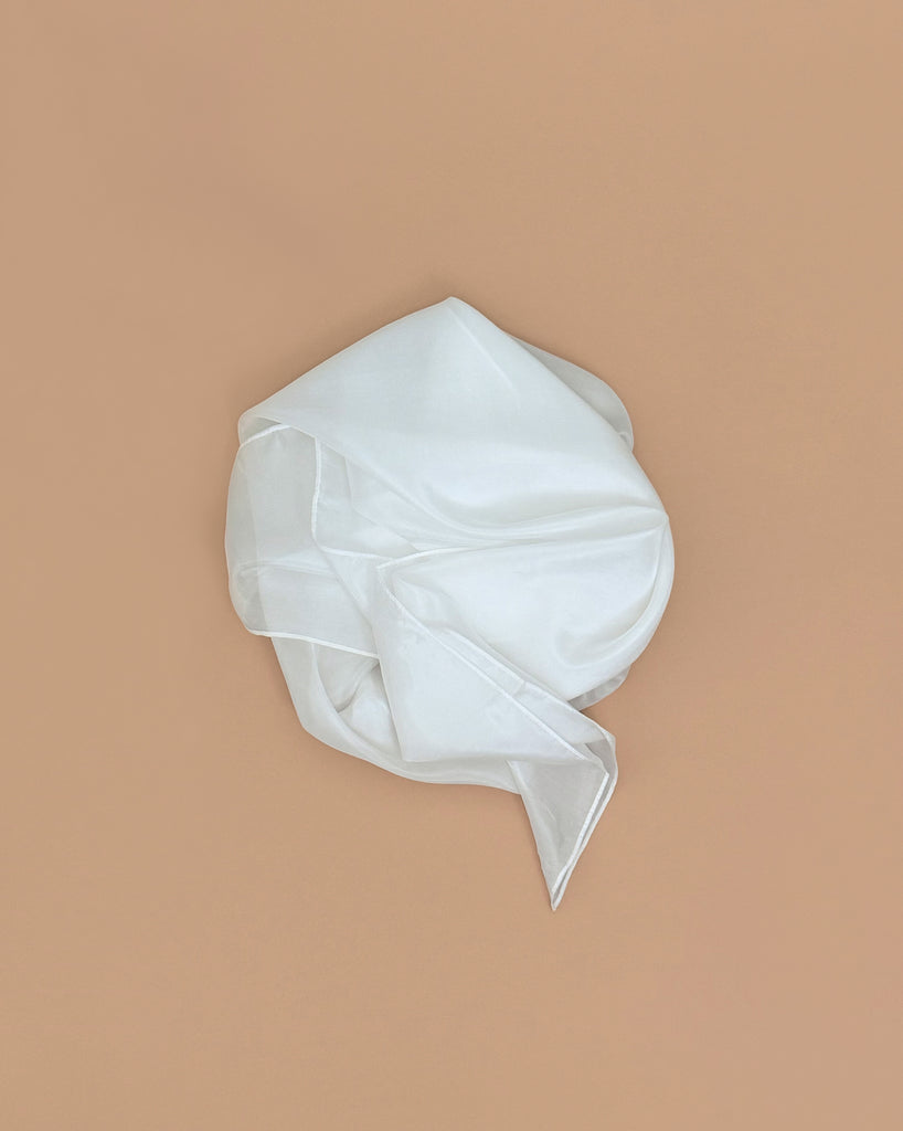 Sarah's Silks Solid Color Playsilk - White: a semi-transparent, 100% pure silk fabric, loosely folded on a plain light brown background. Ideal for open-ended play.