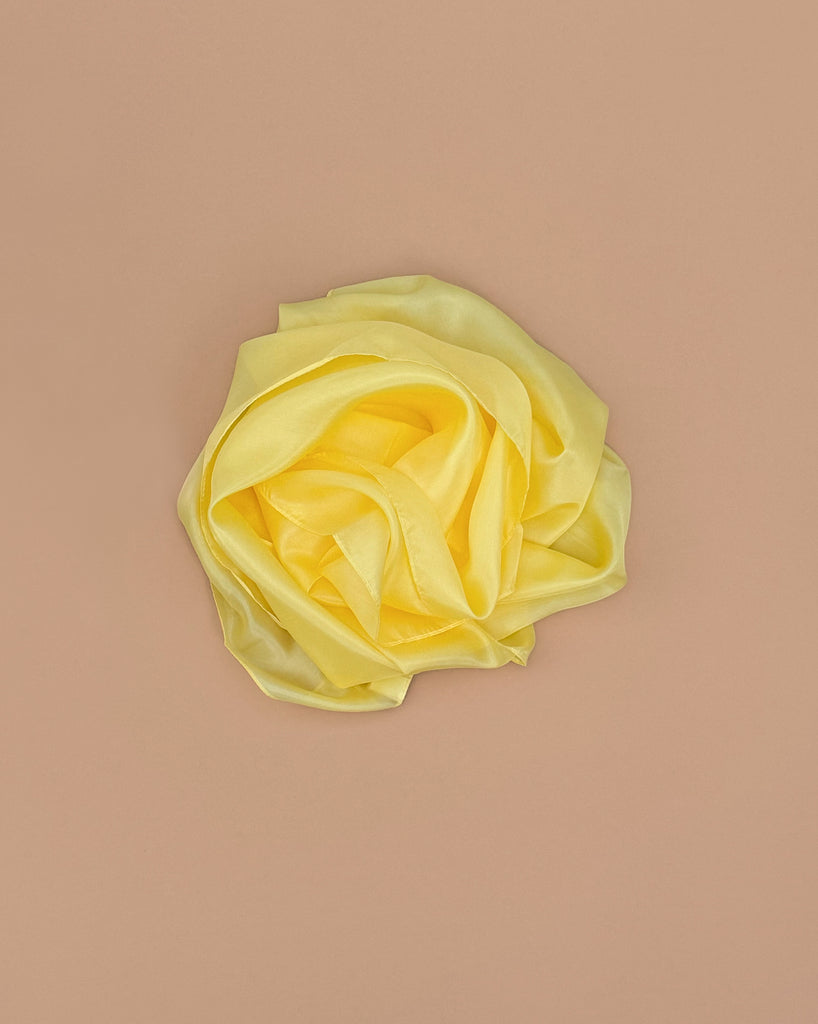The Sarah's Silks Solid Color Playsilk - Sunshine, made from 100% pure yellow silk and artfully shaped like a rose on a beige background, is perfect for open-ended play.