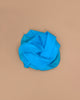 A vibrant turquoise Sarah's Silks Solid Color Playsilk is gently folded atop a neutral beige surface, forming soft curves for a simple, elegant look—ideal for open-ended play.