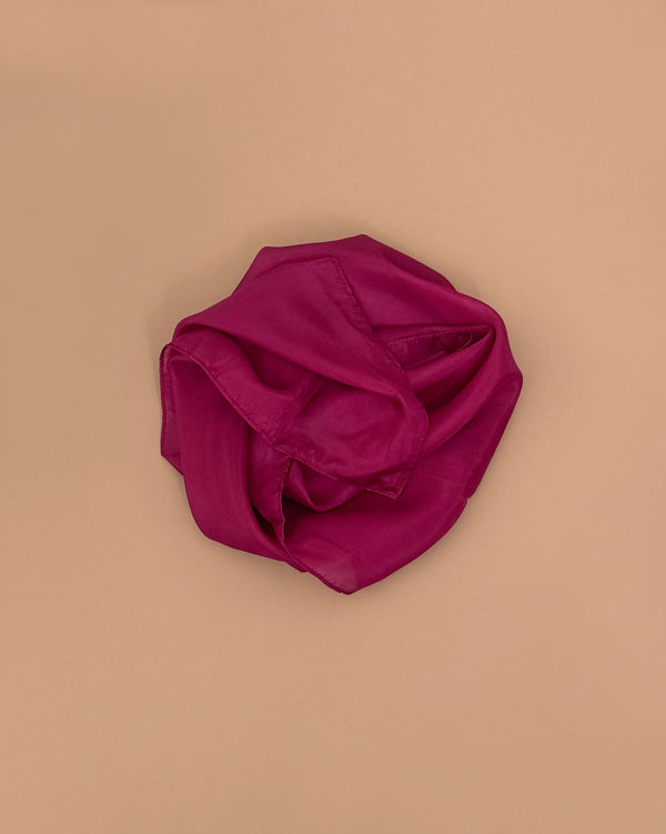 A Sarah's Silks Solid Color Playsilk in Red Violet, made from pure silk, is crumpled and lying on a plain beige background.