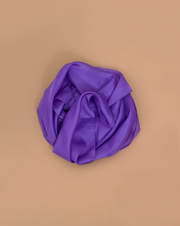 A purple Sarah's Silks Solid Color Playsilk rests crumpled on a flat, light brown surface, viewed from above—capturing the creative spirit of open-ended play.