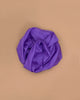 A purple Sarah's Silks Solid Color Playsilk rests crumpled on a flat, light brown surface, viewed from above—capturing the creative spirit of open-ended play.