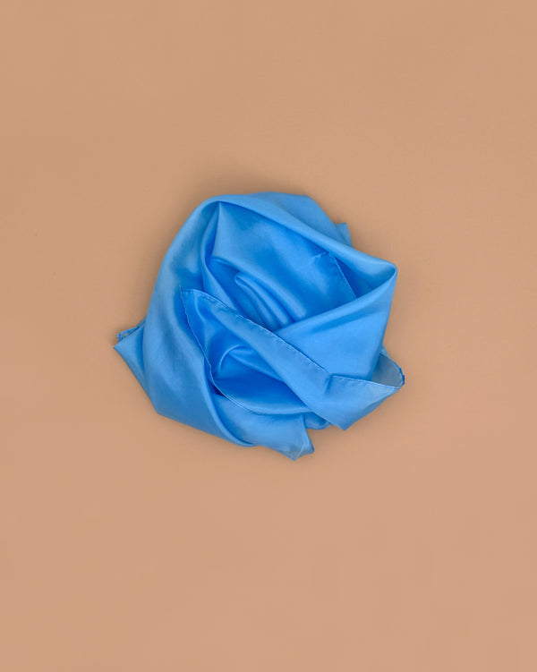 Sarah's Silks Solid Color Playsilk in Sky Blue is carefully folded to look like a rose and displayed on a plain beige background, highlighting its suitability for sensory play.