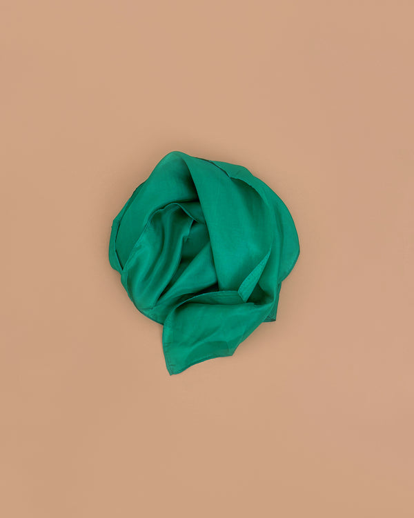 Sarah's Silks Solid Color Playsilk in Emerald, made from pure silk, is loosely folded into a circle and set against a plain light brown background.