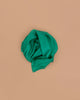 Sarah's Silks Solid Color Playsilk in Emerald, made from pure silk, is loosely folded into a circle and set against a plain light brown background.