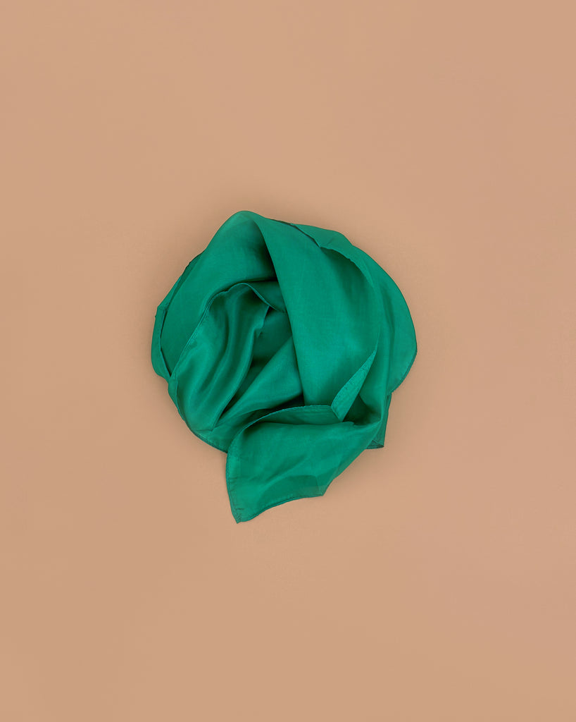 Sarah's Silks Solid Color Playsilk in Emerald, made from pure silk, is loosely folded into a circle and set against a plain light brown background.