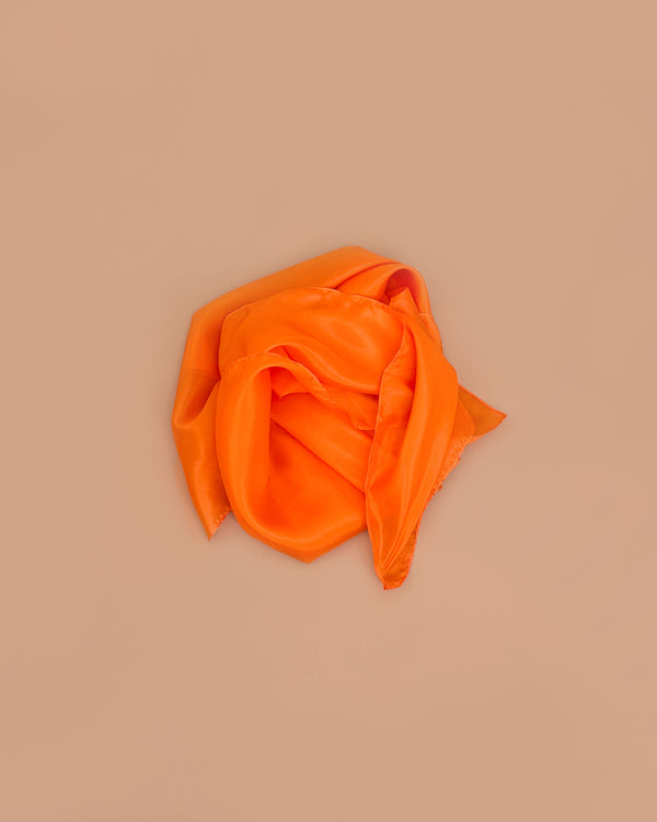Sarah's Silks Solid Color Playsilk in Orange, loosely folded on a light brown background, inspires imaginative, open-ended play and brings elegance to sensory play activities.