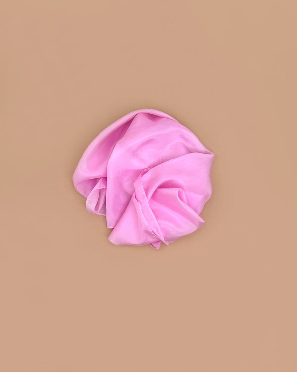 A Sarah's Silks Solid Color Playsilk in pink, made from pure silk and perfect for open-ended play, lies crumpled on a smooth, solid light brown background.