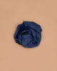 A Sarah's Silks Giant Playsilk - Midnight, with deep navy blue satin reminiscent of open-ended play, is crumpled and set on a plain light brown surface.