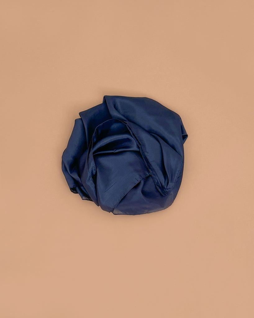 A Sarah's Silks Giant Playsilk - Midnight, with deep navy blue satin reminiscent of open-ended play, is crumpled and set on a plain light brown surface.