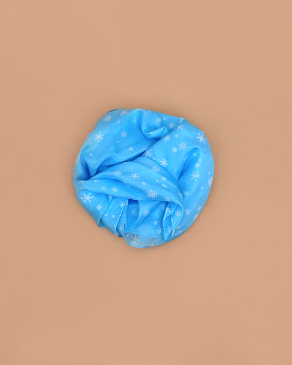 A Sarah's Silks Giant Playsilk - Snow headwrap, light blue with white snowflakes, is displayed in a circle on a beige background, encouraging imaginative play inspired by Waldorf toys.