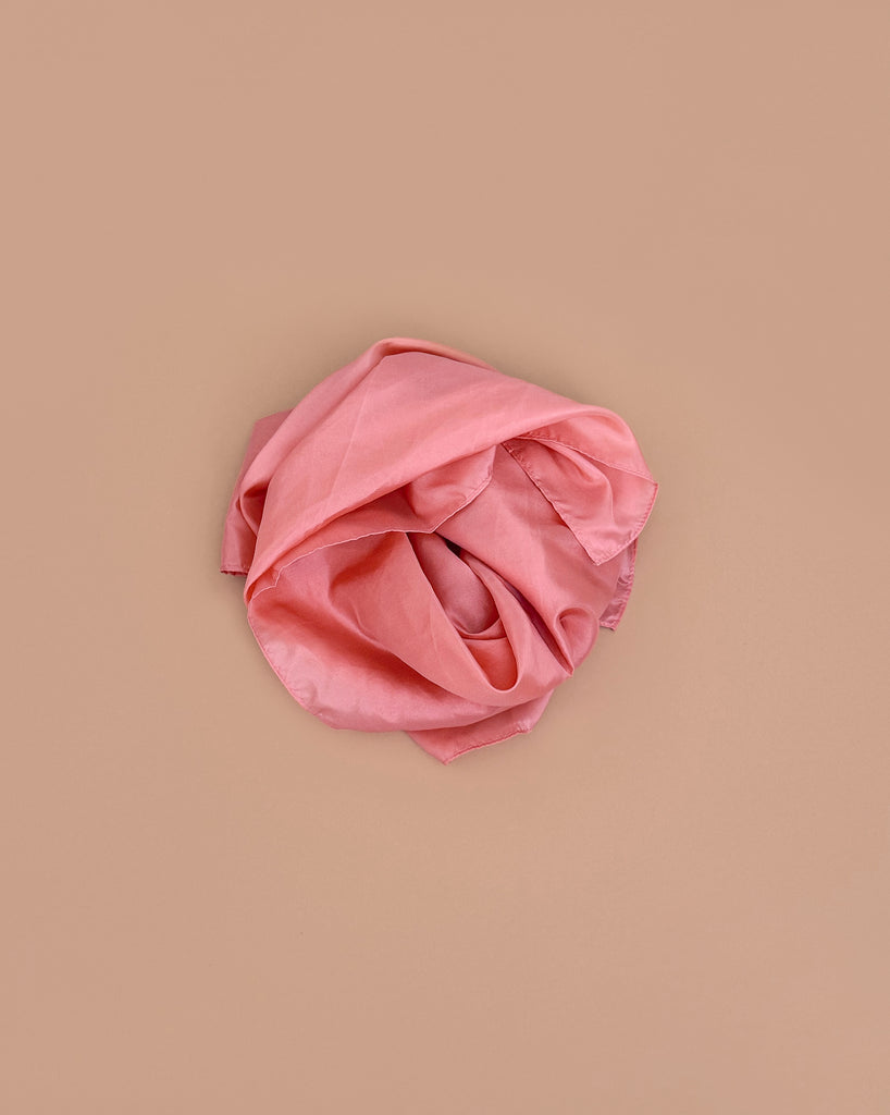 Sarah's Silks Solid Color Playsilk in Peach, perfect for sensory play, is softly crumpled and arranged in a loose circle on a light brown background.