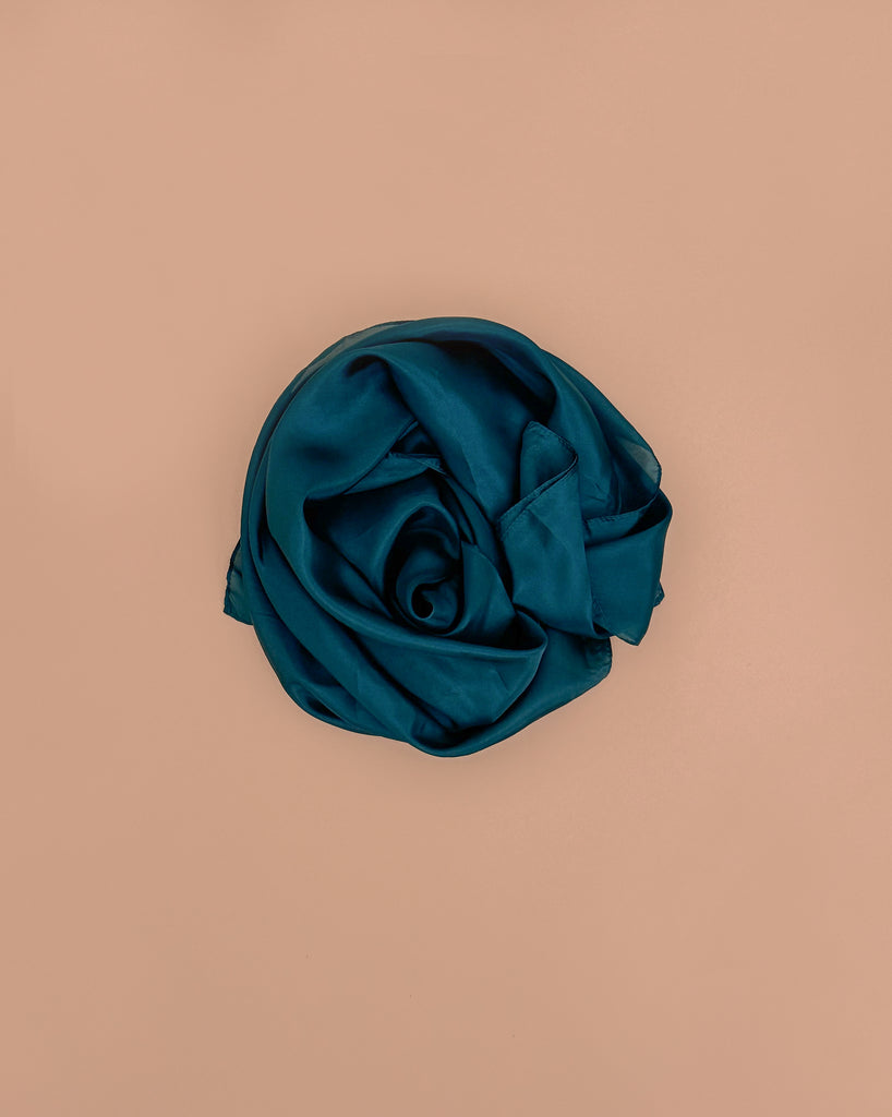 Sarah's Silks Giant Playsilk - Evergreen is artfully rolled into a circle and displayed on a simple beige background.