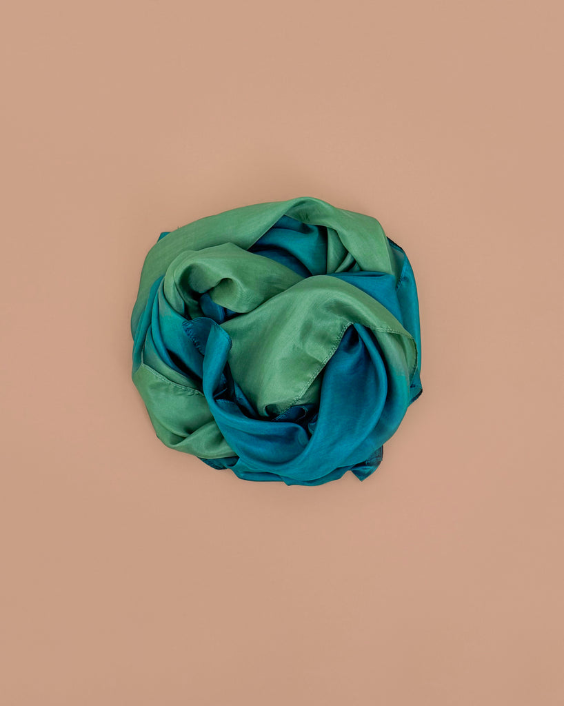 Sarah's Silks Giant Playsilk - Forest, in green and teal, is loosely rolled into a circle and displayed on a plain beige background, perfect for imaginative play.