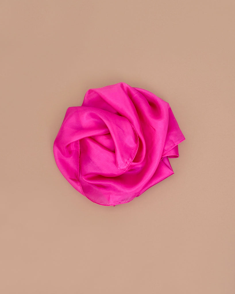 Sarah's Silks Solid Color Playsilk - Rose is neatly rolled in a circle on a plain beige background, inviting open-ended play and sensory exploration.