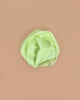 Sarah's Silks Solid Color Playsilk - Lime, a silky light green scarf, is rolled in a circle on a plain light brown background—ideal for open-ended and sensory play.