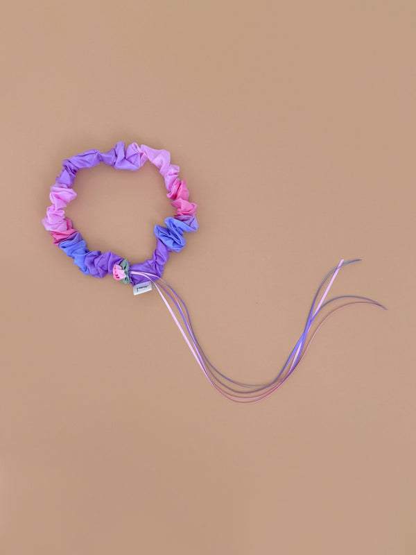 Sarah's Silks Garland Headband - Blossom features pink and purple fabric with a small flower embellishment and long, matching ribbons—perfect for dress-up—shown on a simple beige background.