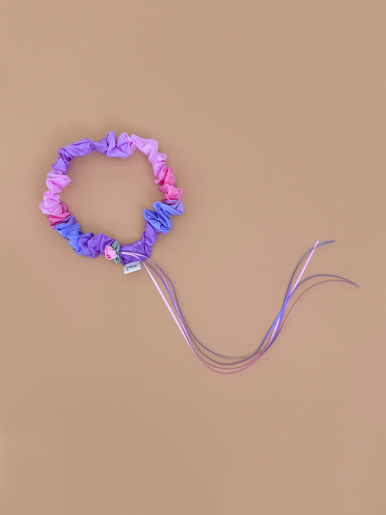 Sarah's Silks Garland Headband - Blossom features pink and purple fabric with a small flower embellishment and long, matching ribbons—perfect for dress-up—shown on a simple beige background.