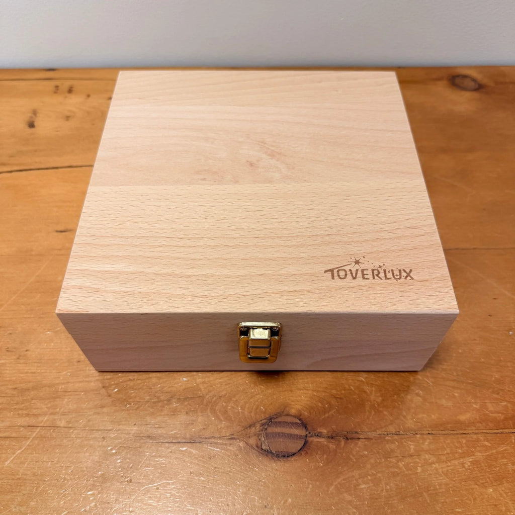 The Toverlux Silhouette Storage Box Deluxe is a light wooden box with a gold-colored latch, featuring "TOVERLUX" and stars engraved on the lid—perfect for organizing your Toverlux Silhouettes.