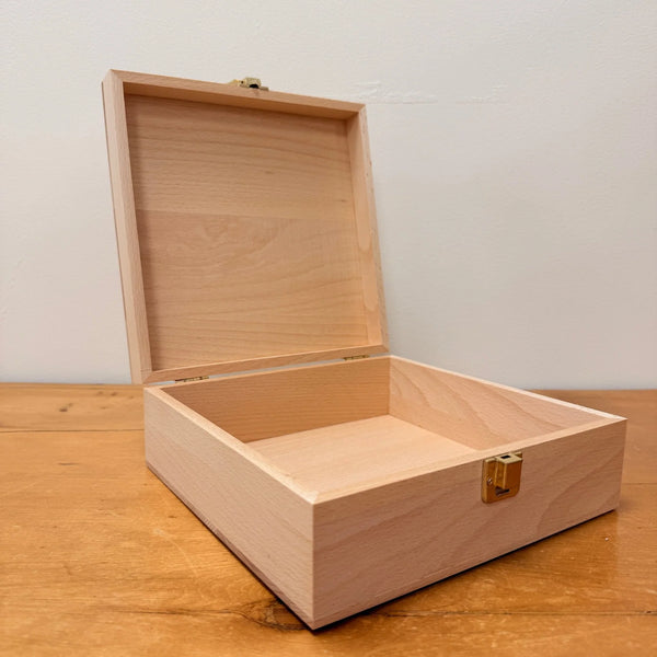 The Toverlux Silhouette Storage Box Deluxe is a light wooden box with a hinged lid and gold-colored clasps, perfect for organizing Toverlux Silhouettes. It stands open on a wooden surface against a plain white wall.