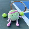 The Mon Ami - Tina Tennis Ball Plush Toy, featuring a pink headband, striped limbs, and a smiling face, sits on the court near tennis balls and a racket—a perfect plush for young sports fans!.