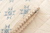 A close-up of the Organic Cotton Baby Star Quilt - Sky, a cream-colored baby quilt with blue star patterns and scalloped trim, resting on a matching quilted surface. Ships in one week.