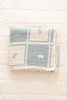 The Organic Cotton Patchwork Baby Blanket - Spring Bloom features a blue and white checkered pattern, small embroidered flowers, and crochet trim, shown folded on a white quilted surface.