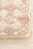 A close-up of the Organic Cotton Baby Patchwork Blanket - Pink Bows, featuring soft quilted cotton in beige and light pink with a diamond pattern, lace trim, and delicate details—perfect as a baby blanket. Ships in one week.