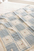 The Organic Cotton Patchwork Baby Blanket - Spring Bloom features soft, quilted organic cotton in blue and cream squares with embroidered pink flowers, displayed atop a lightly patterned bedspread.