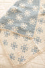 The Organic Cotton Baby Star Quilt - Sky features a blue and cream star pattern, textured quilted design, and delicate crochet trim. It’s folded on a cream surface.