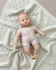 A Minikane Soft Body Doll (11") - Jasper, dressed in a light-colored onesie, lies on a textured, light gray blanket. The doll features a bald head, wide eyes, and a slightly open mouth. Crafted from phthalate-free vinyl for safety and comfort, Jasper makes for the perfect bedtime companion in this soft and cozy setting.