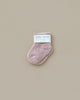 A pair of Baby Pile Knit Socks in pale pink is displayed against a neutral beige background. The fluffy, small socks are neatly folded, with a white label reading "baby socks" and "Newborn" visible on top.