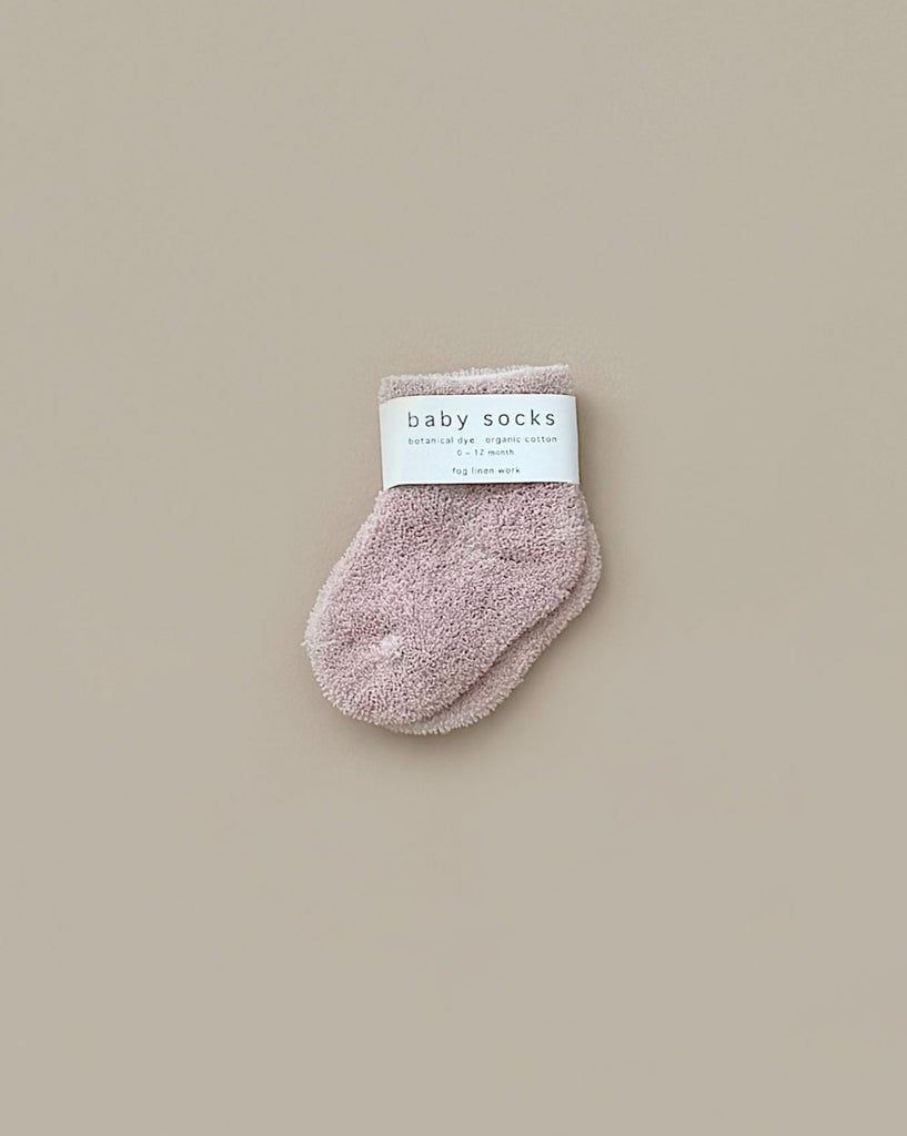 A Newborn Gift Set - Pink featuring soft baby socks with a white "baby socks" label, displayed on a beige background—an ideal addition to gifts like the Grimm's Small Wooden Rainbow or Let's Go Explore Book.