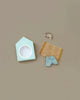 The Maileg Beach Bundle for Big Brother features a light blue beach hut box, a brown and white striped towel, a blue gingham cloth, and a tiny transparent beach bag with gold handles—perfect vacation accessories on a beige background.