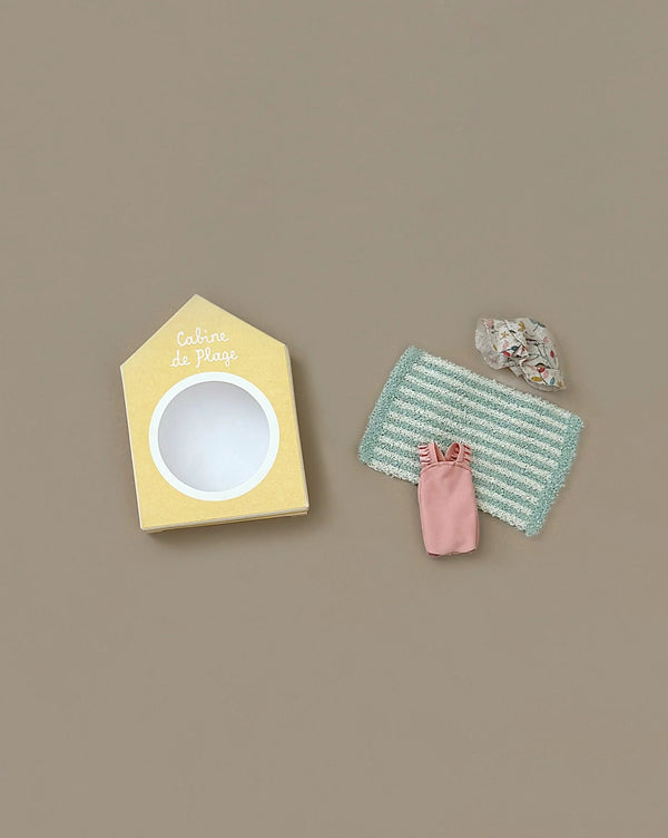 The Maileg Beach Bundle for Big Sister includes a yellow house-shaped box labeled "Cabine de Plage," a striped mat, a pink dress, and patterned beach accessories for mice, perfect for beach fun with your big sister mouse.