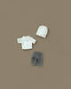 The Maileg Extra Clothing: Chef Clothes For Big Sister And Big Brother Mouse set features a white chef’s hat and jacket with black-and-white checkered pants, displayed on a plain brown background.