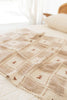 The Organic Cotton Baby Blanket - Pony, featuring beige and cream patchwork with an embroidered pony and crochet trim, is displayed on a white quilted bed in a softly lit bedroom.