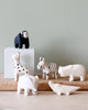 Displayed on a light wooden surface against a pastel green background is a collection of handcrafted wooden animals. The handmade animal toys include a black-and-white monkey, giraffe, zebra, rhinoceros, elephant, and crocodile. Among the group, the giraffe and zebra display intricate black markings. These charming pieces are part of the Handmade Tiny Wooden Safari Animals collection – Rhino.