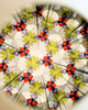 Peer through the Konges Sloejd Kaleidoscope - Like Cats and Dogs to discover a mesmerizing, symmetrical pattern of green, red, and purple shapes—reminiscent of leaves and jewels—arranged in a repeating geometric design, highlighted with vibrant pearl-like accents.